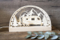 Preview: LED-Schwibbogen aus Holz mit Wohnwagen-Motiv vor Bergkulisse mit Sonne, Sternen und Tannen, davor Campingstühle und Tisch, warmweiß beleuchtet, mit Schriftzug „Camperleben" auf der Holzleiste